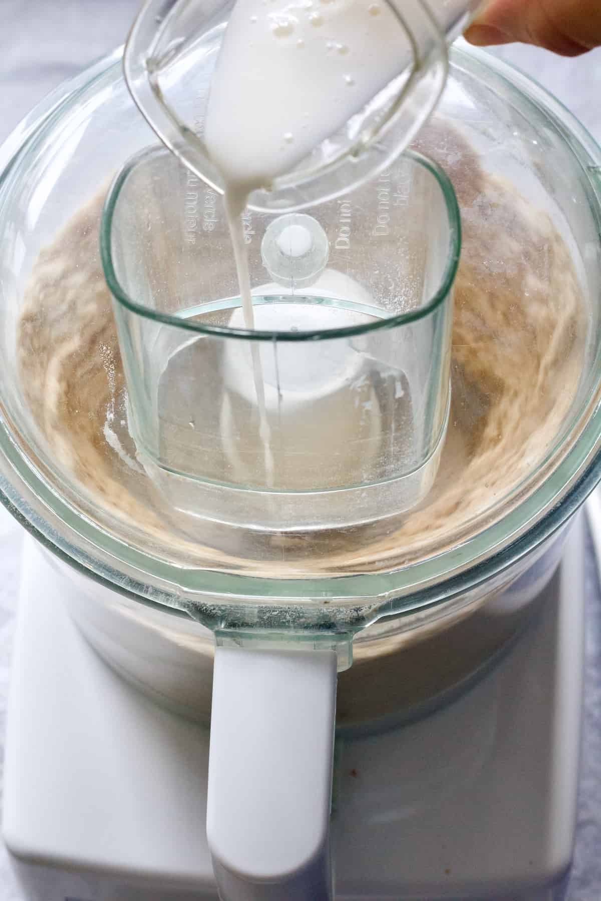 Milk being poured into food processor to bind the pastry.