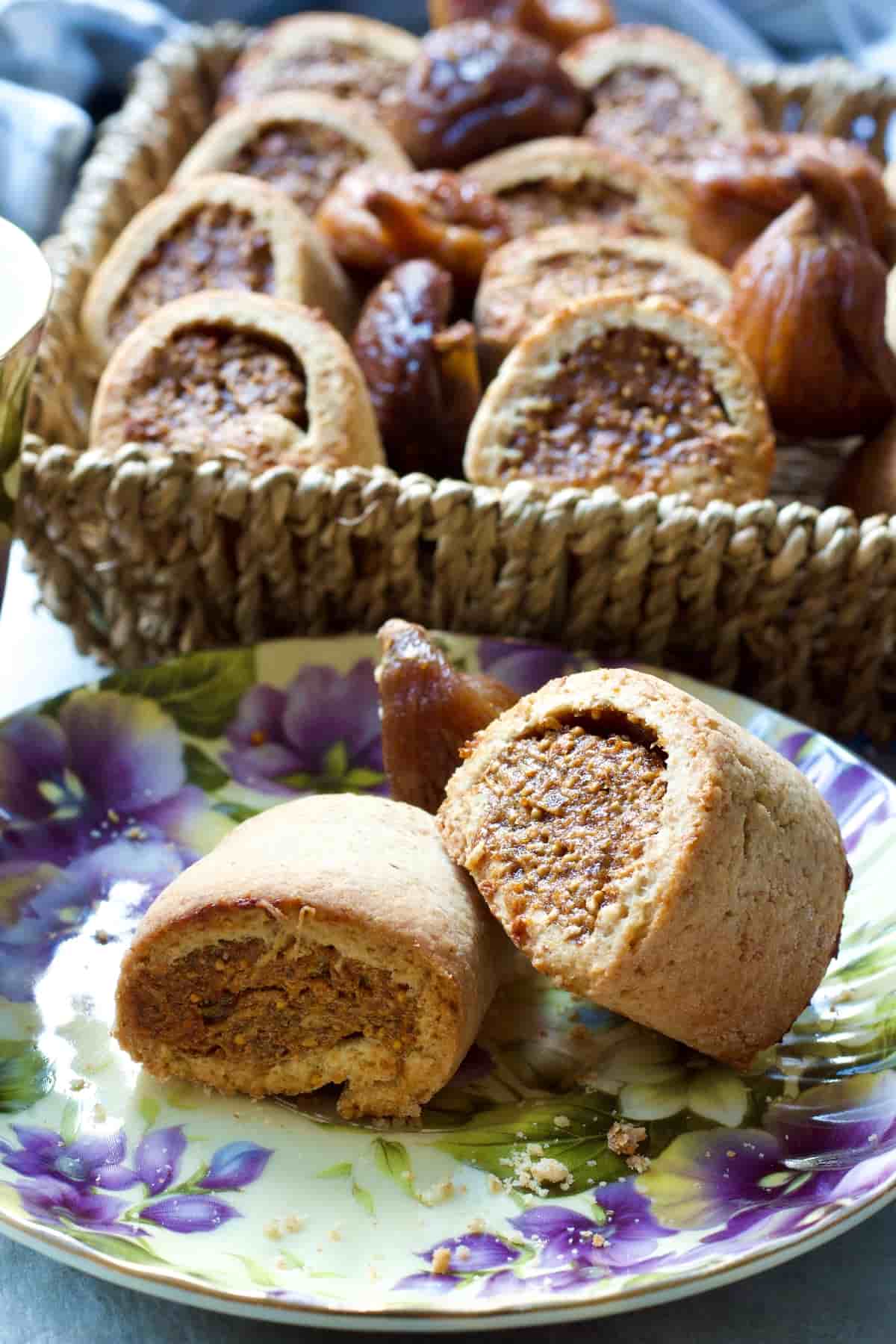 Two fig rolls on a plate with basket full of fig rolls behind.