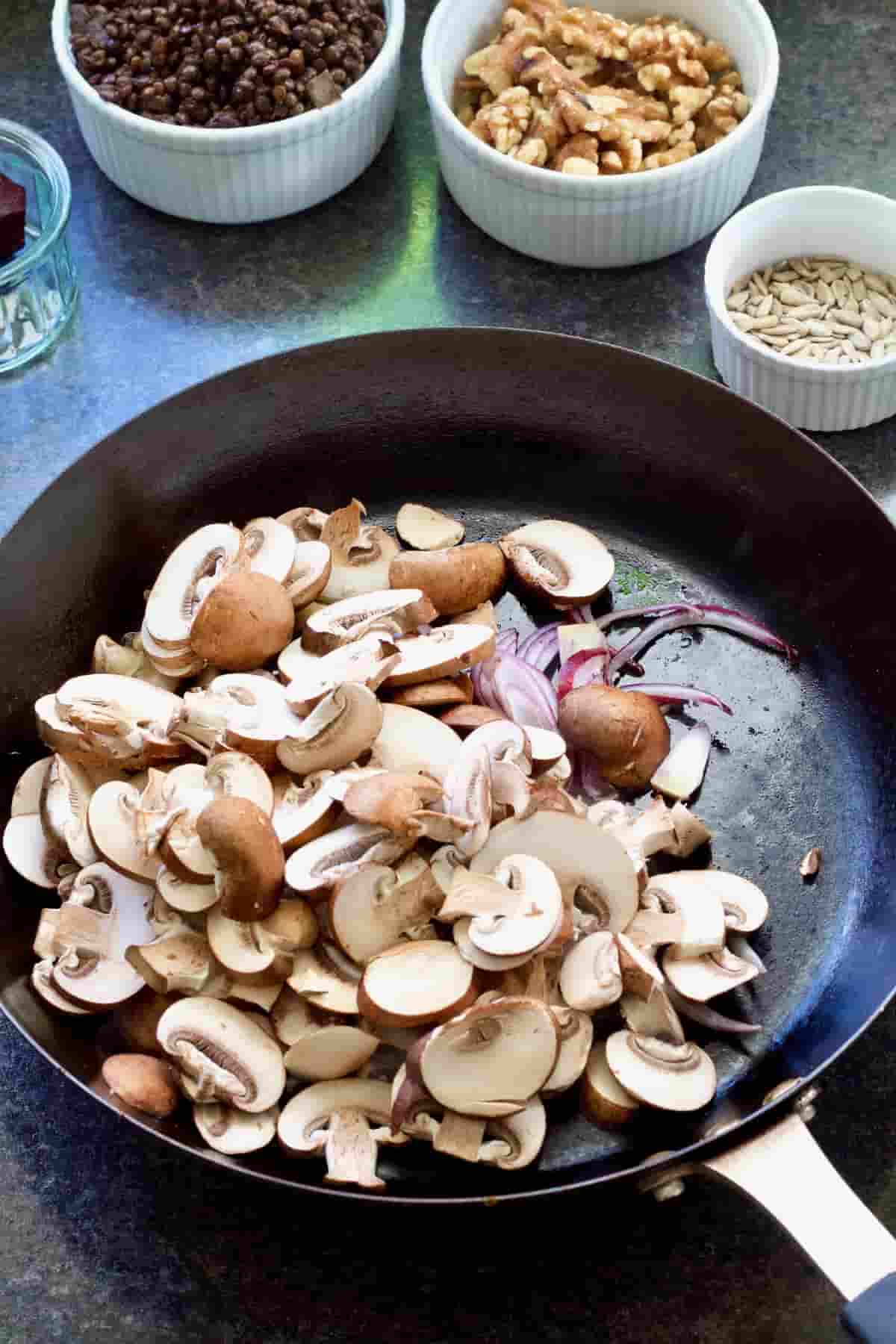 Mushrooms and sliced red onions in a frying pan.