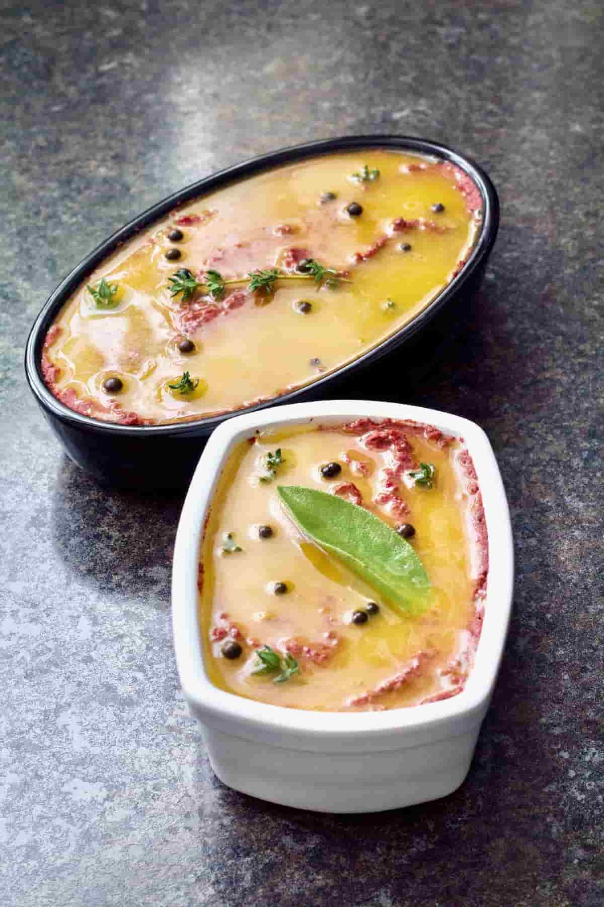 Mushroom and walnut pâté in two dishes, garnished with herbs and melted butter.