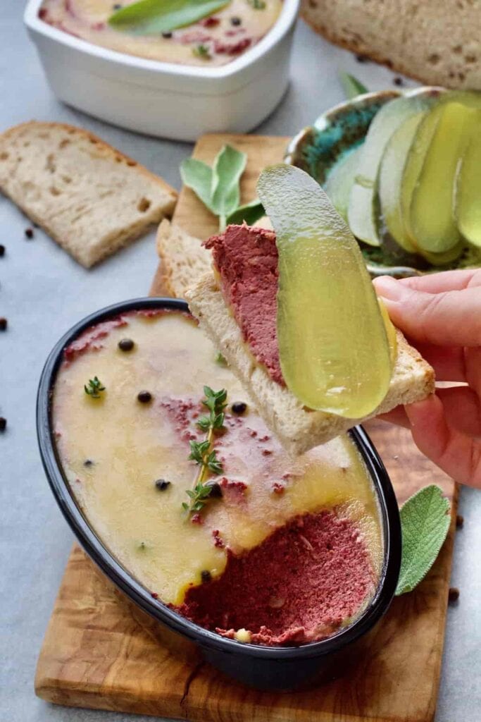 Hand holding piece of bread with pâté and a gherkin.