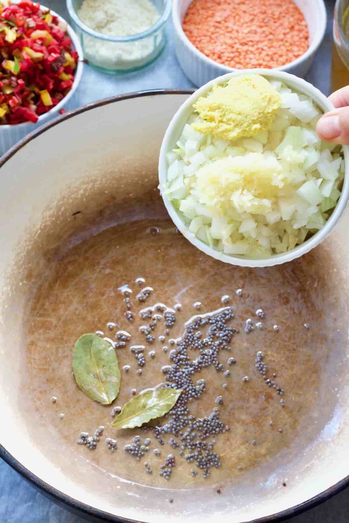 Chopped onion, garlic and ginger being added to the pot with mustard seeds & bay leaves.