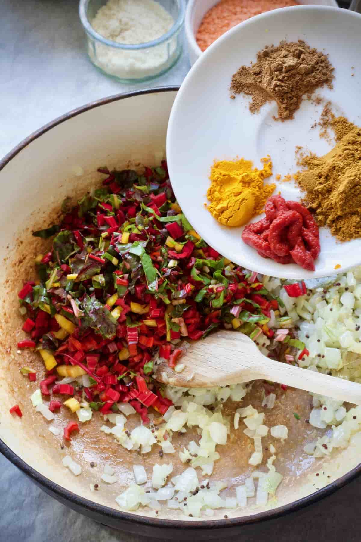 Spices being added to the pot with some sautéed veg.