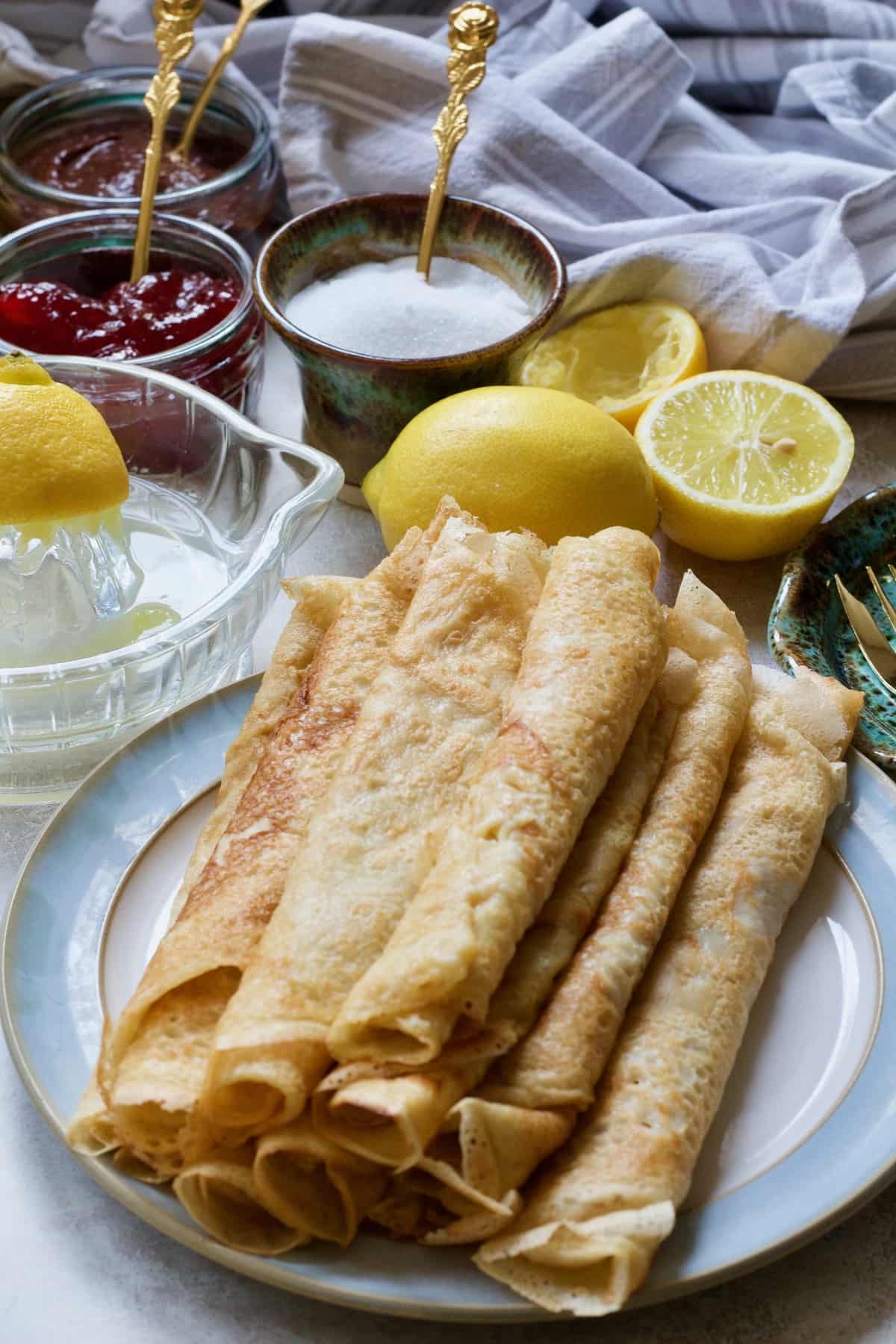 Rolled vegan pancakes on a plate surrounded by toppings.