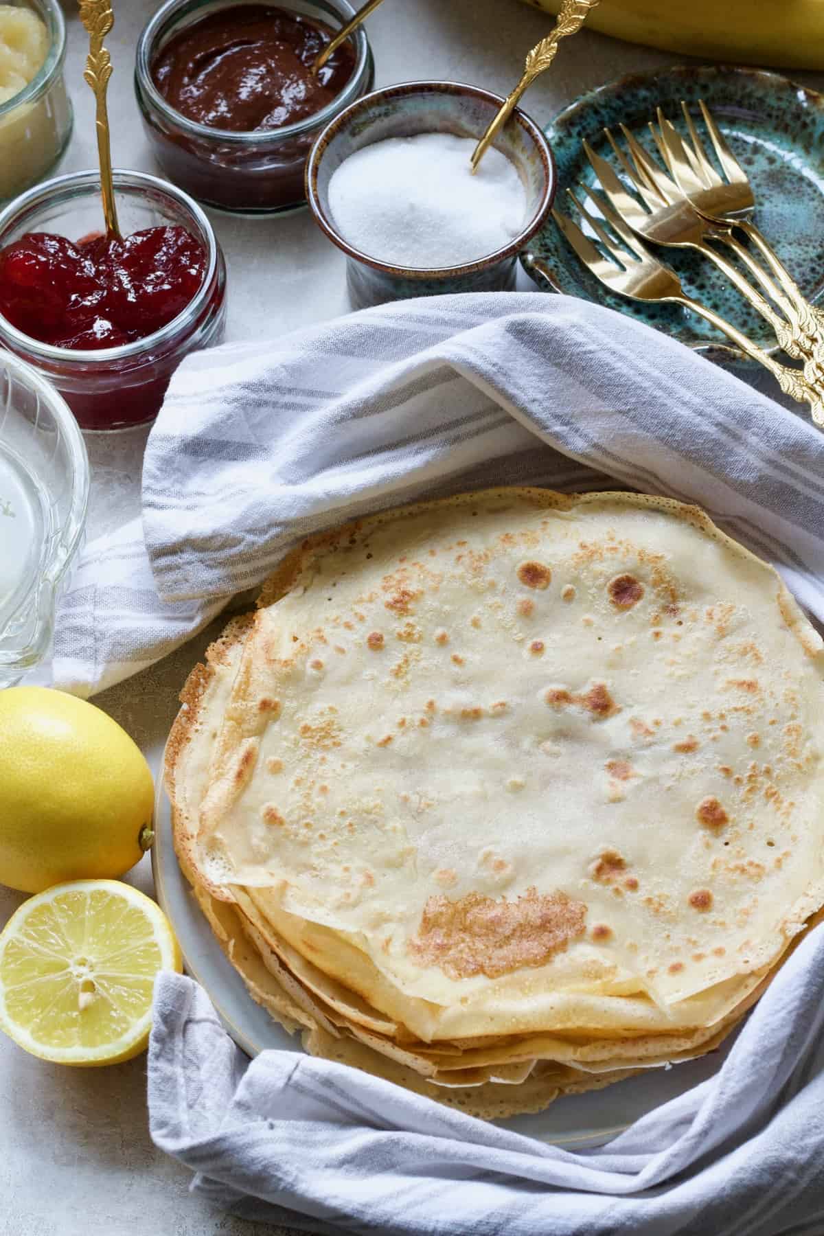 Cooked vegan pancakes (crepes) on a plate, toppings & forks.