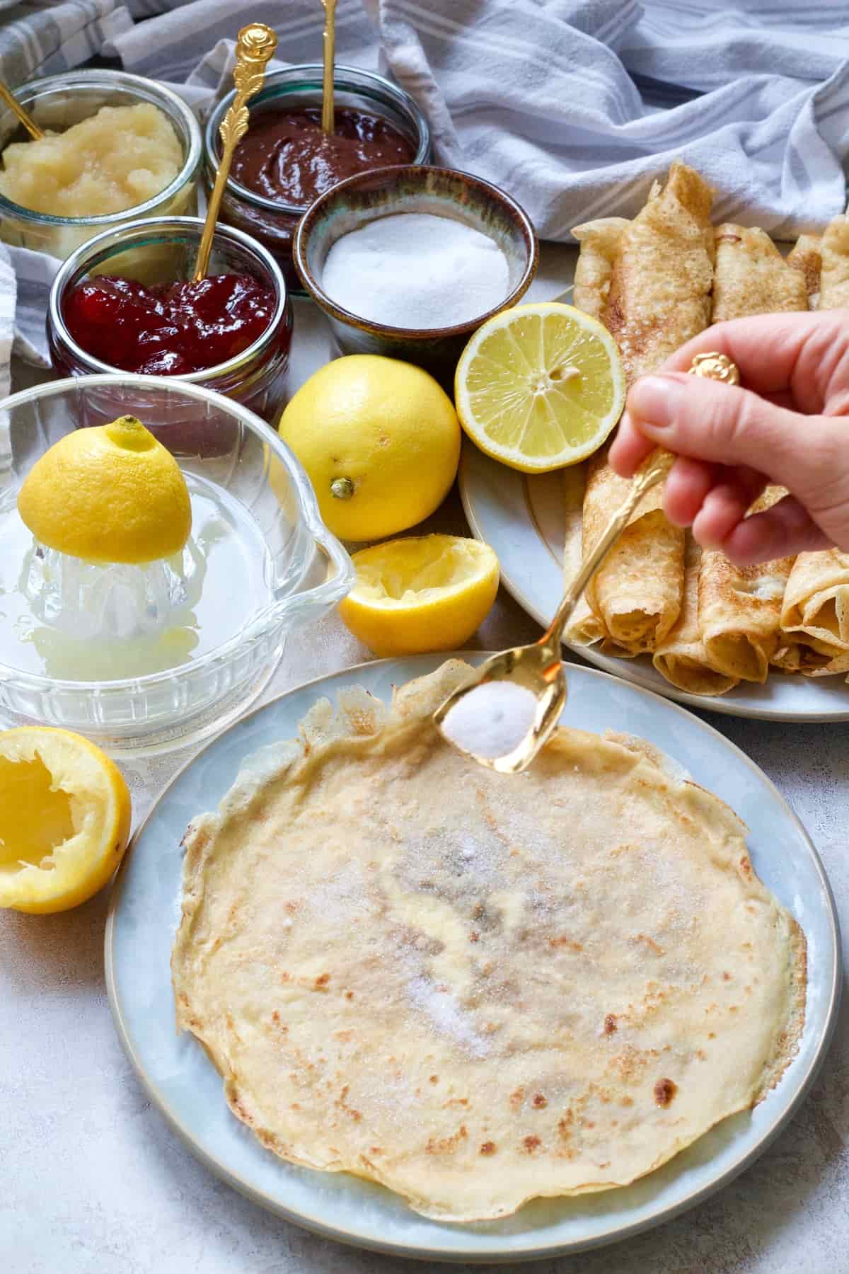 Hand sprinkling sugar over vegan pancake.