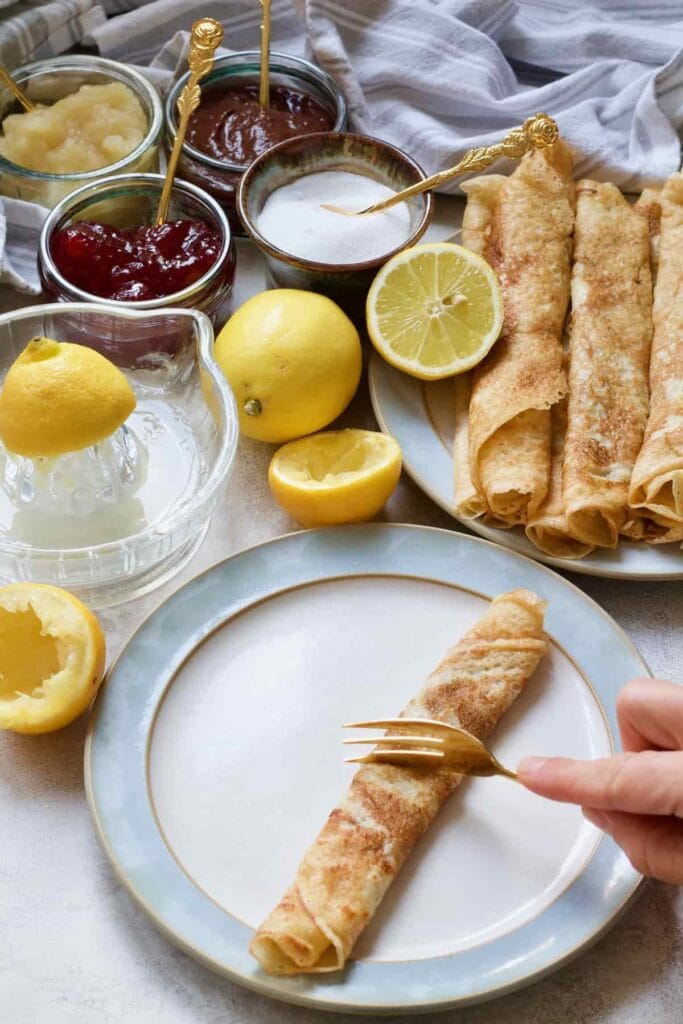 Hand cutting rolled pancake in half with a fork.