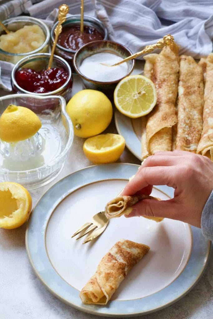 Hand holding half a rolled vegan pancake over a plate.