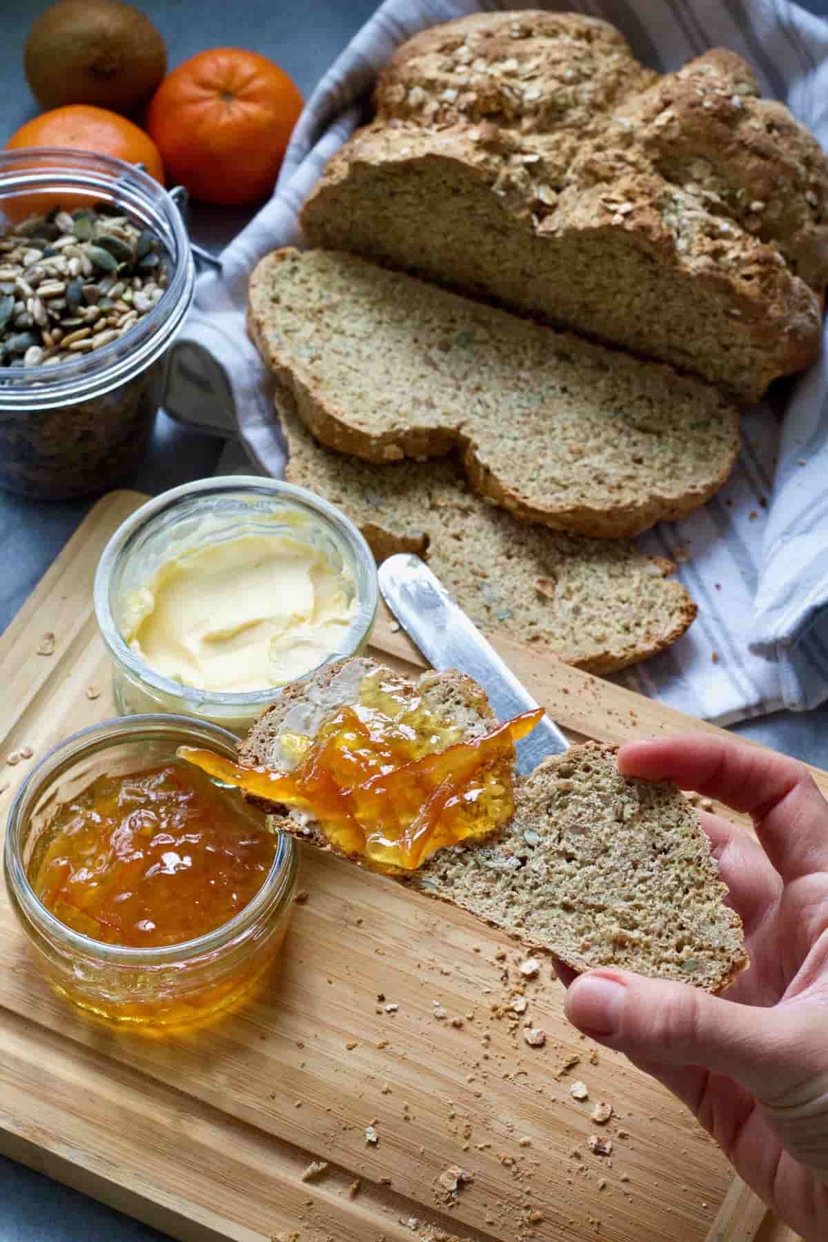 Hand holding slice of bread half of which is topped with marmalade.