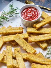 Pile of baked polenta chips with rosemary and bowl of ketchup.
