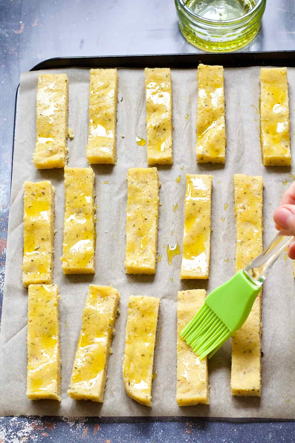 Polenta chips being brushed with oil before baking.
