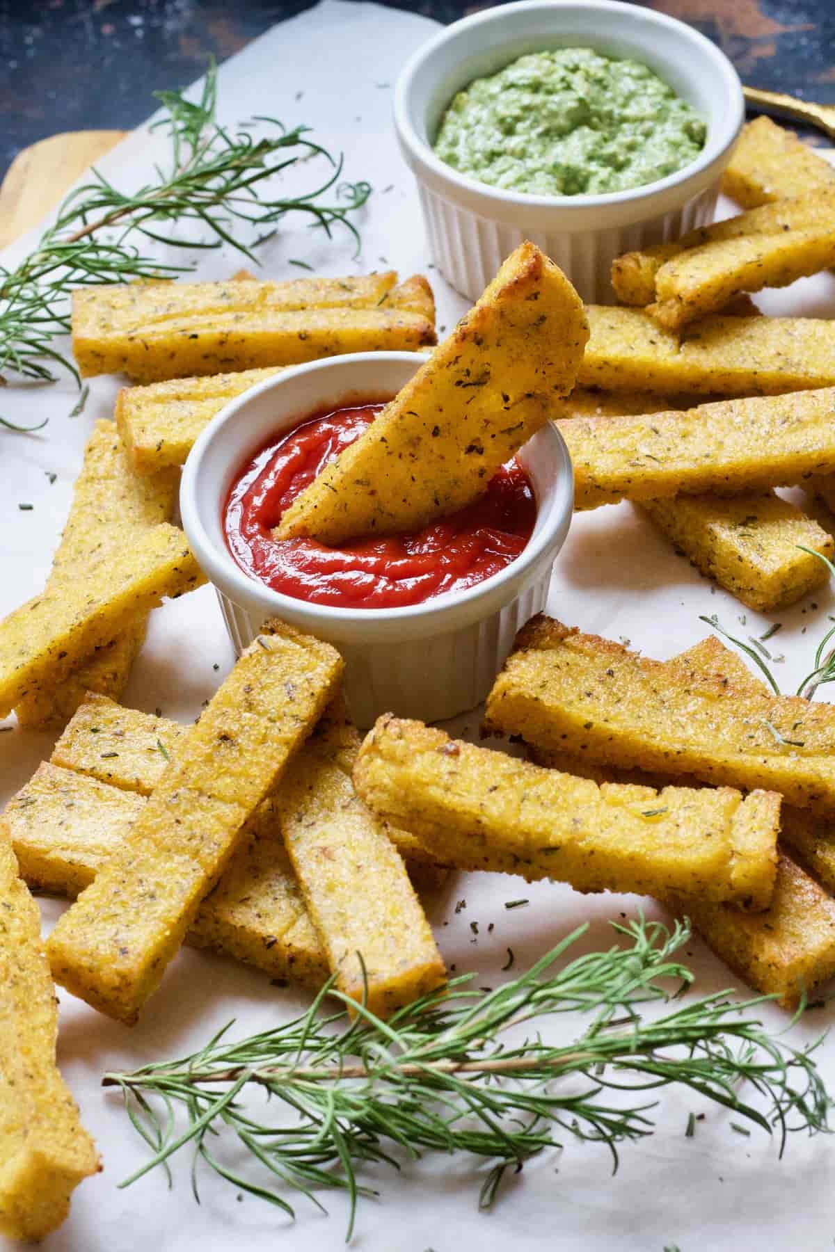 Polenta chip in a bowl of ketchup with more chips around.