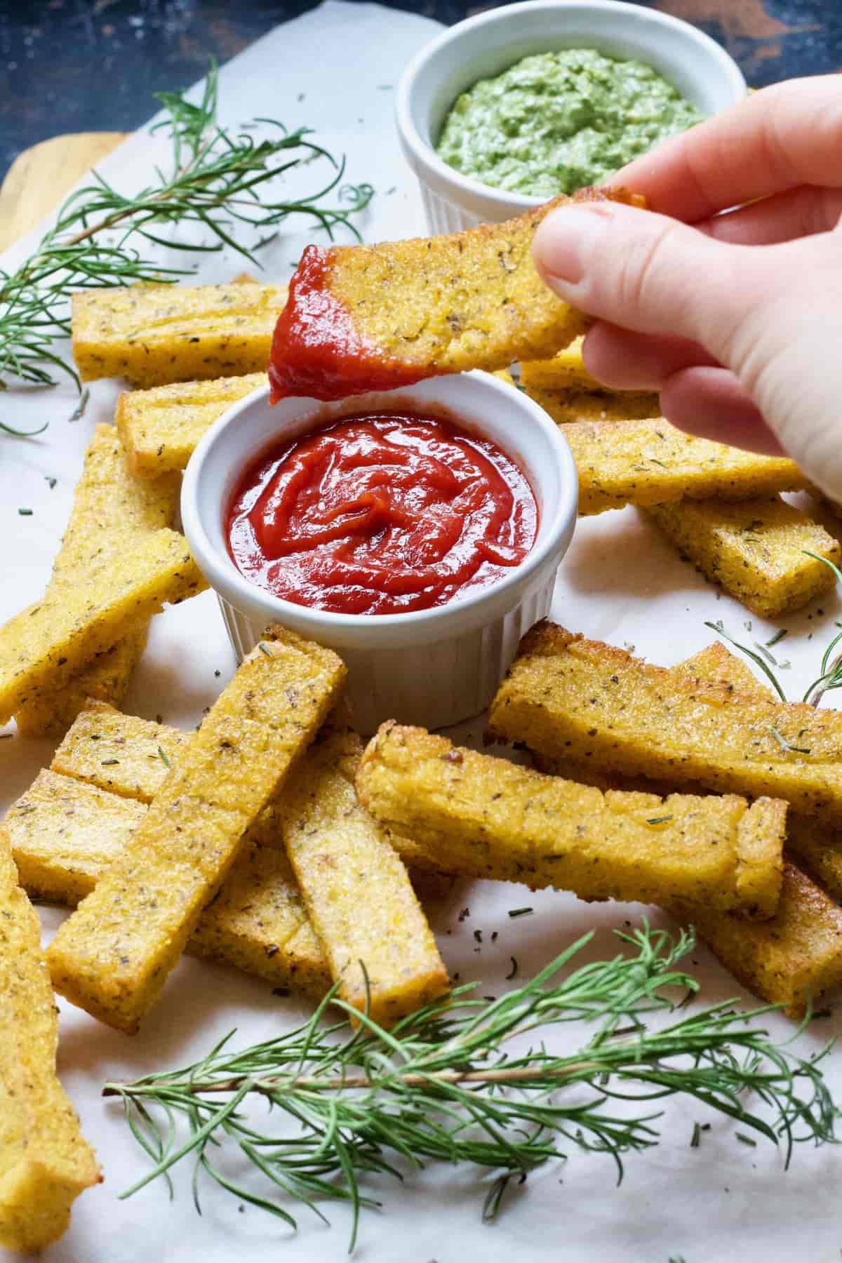 Hand dipping polenta chip in ketchup.