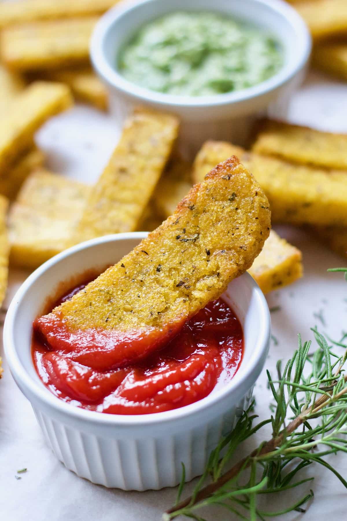 Polenta chip in a bowl of ketchup (close up).