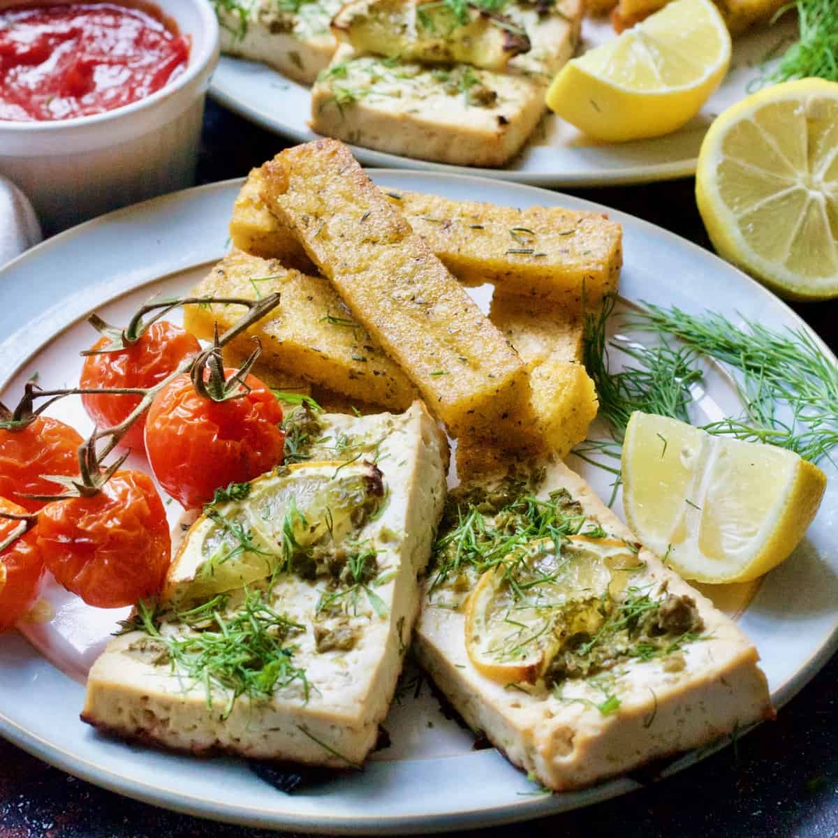 Two slices of tofu fish, polenta chips and roasted tomatoes.
