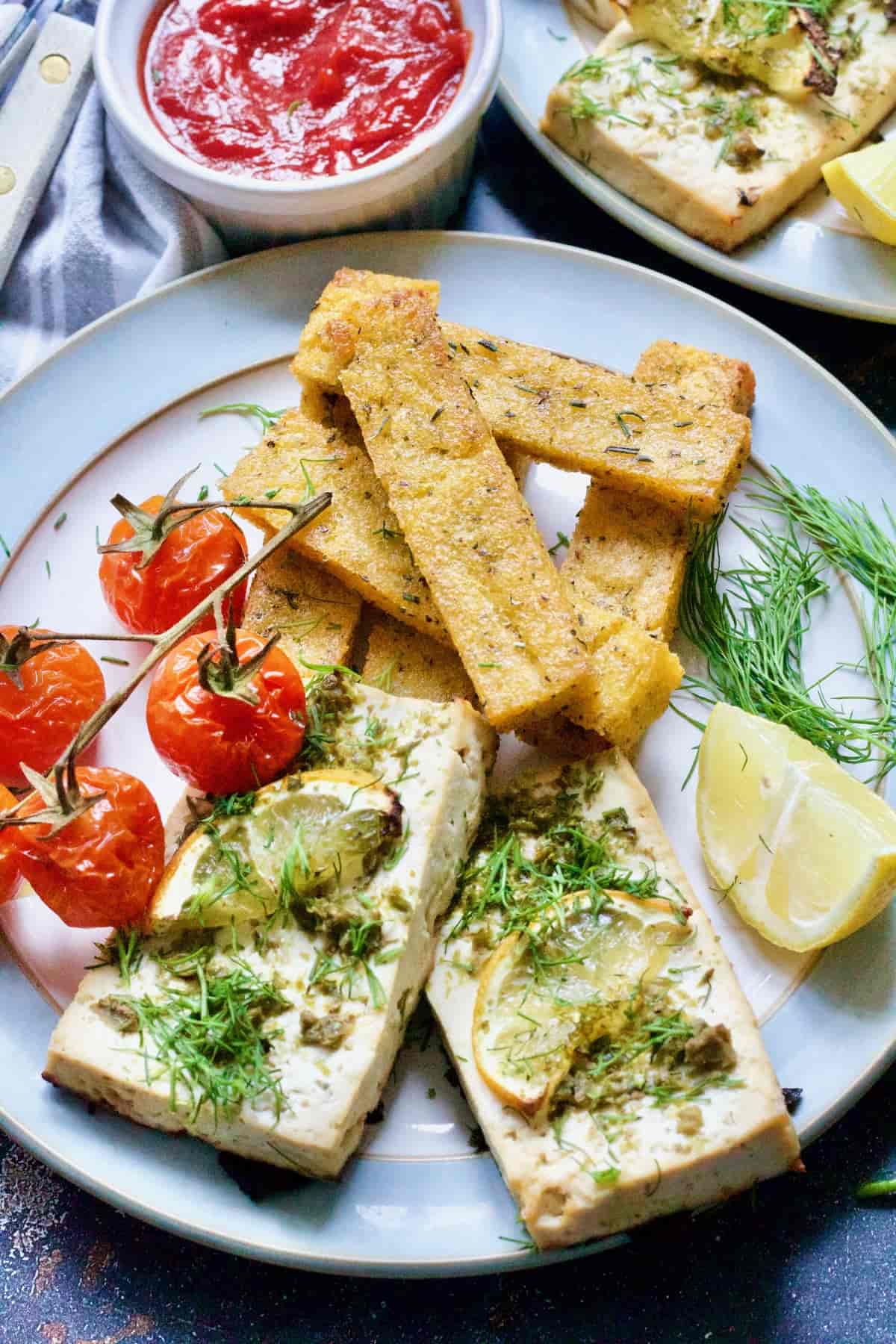 Plate with vegan tofu fish, polenta chips & roasted tomatoes.