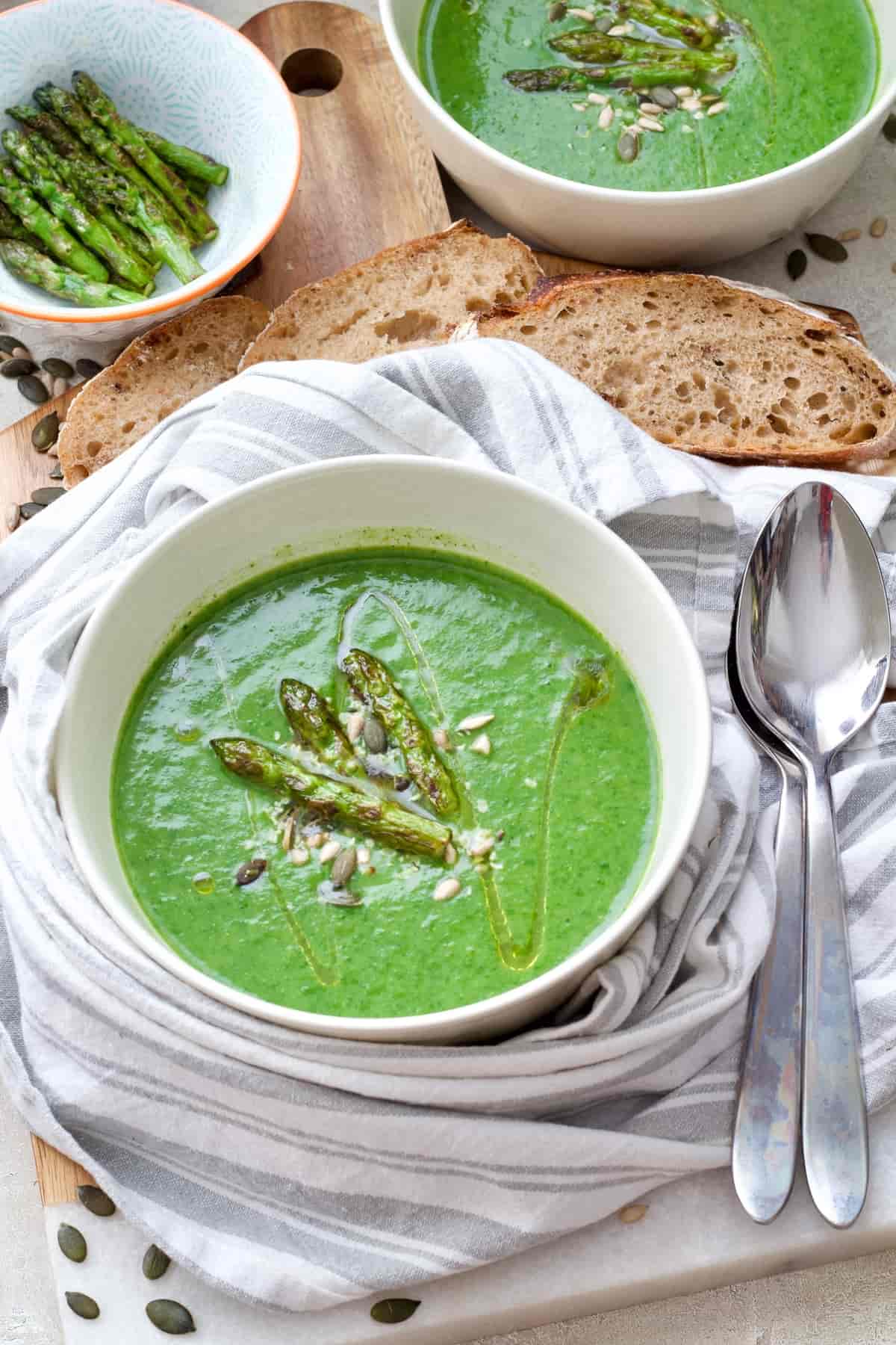 Bowl of green soup wrapped with towel, spoons on the side.
