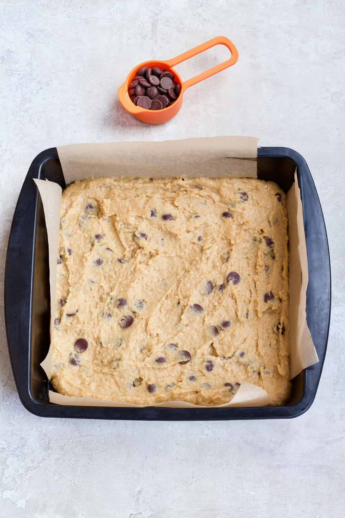 Chickpea blondies in baking tin with extra chocolate chips in a cup.