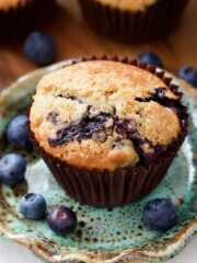 Vegan blueberry muffin on a plate with blueberries around it.