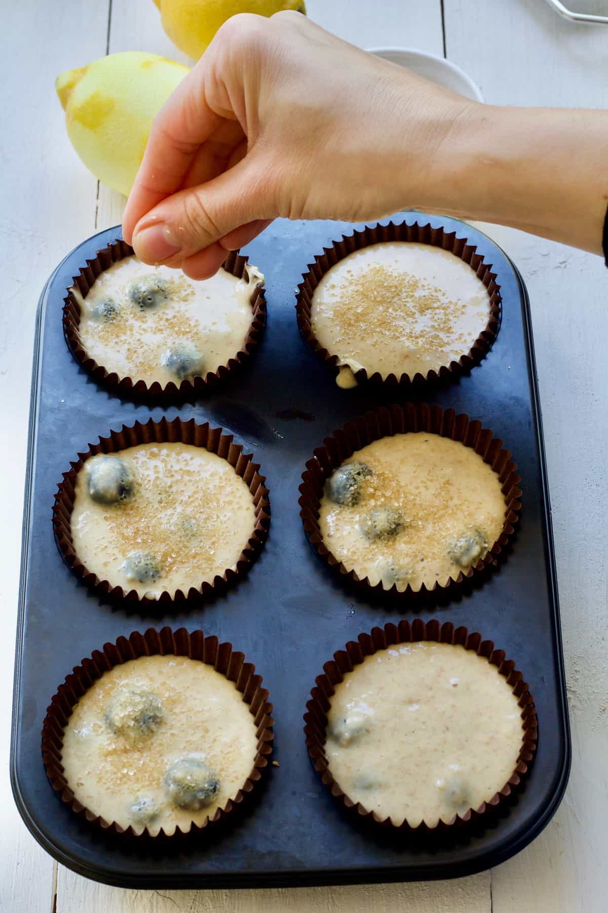 Hand sprinkling sugar over unbaked muffins.