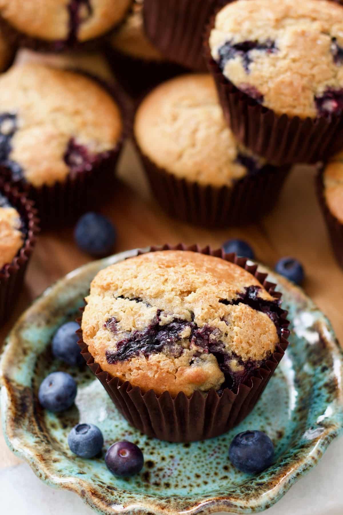 Blueberry muffin on a plate with more muffins behind it.