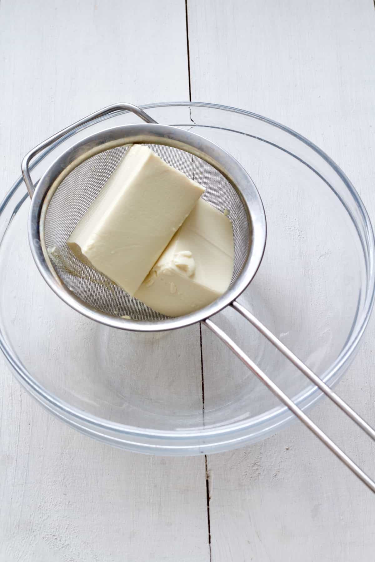 Silken tofu draining on a sieve over a bowl.