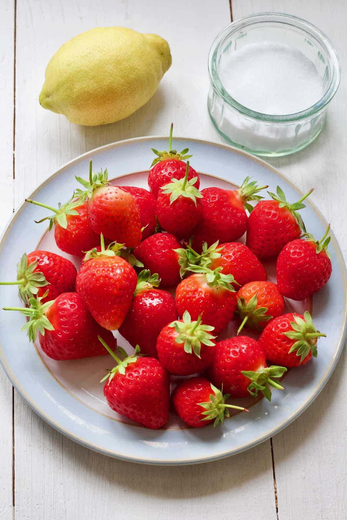 Fresh strawberries on a plate, lemon & bowl with sugar.
