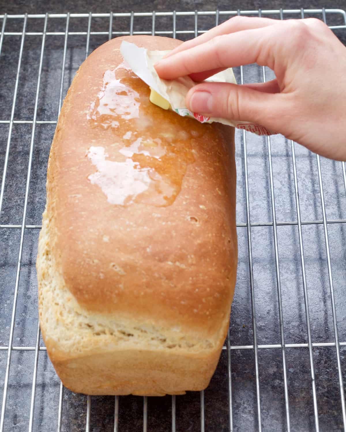 Butter being rubbed over the top of hot bread loaf.