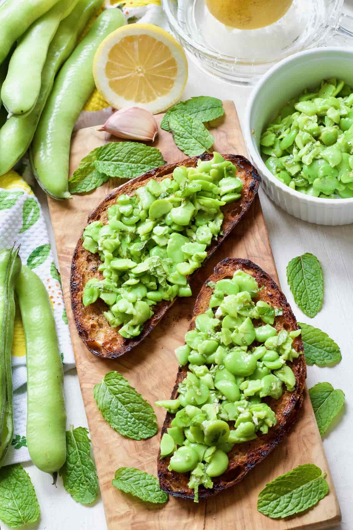 Two broad bean bruschettas on board with fresh mint leaves.