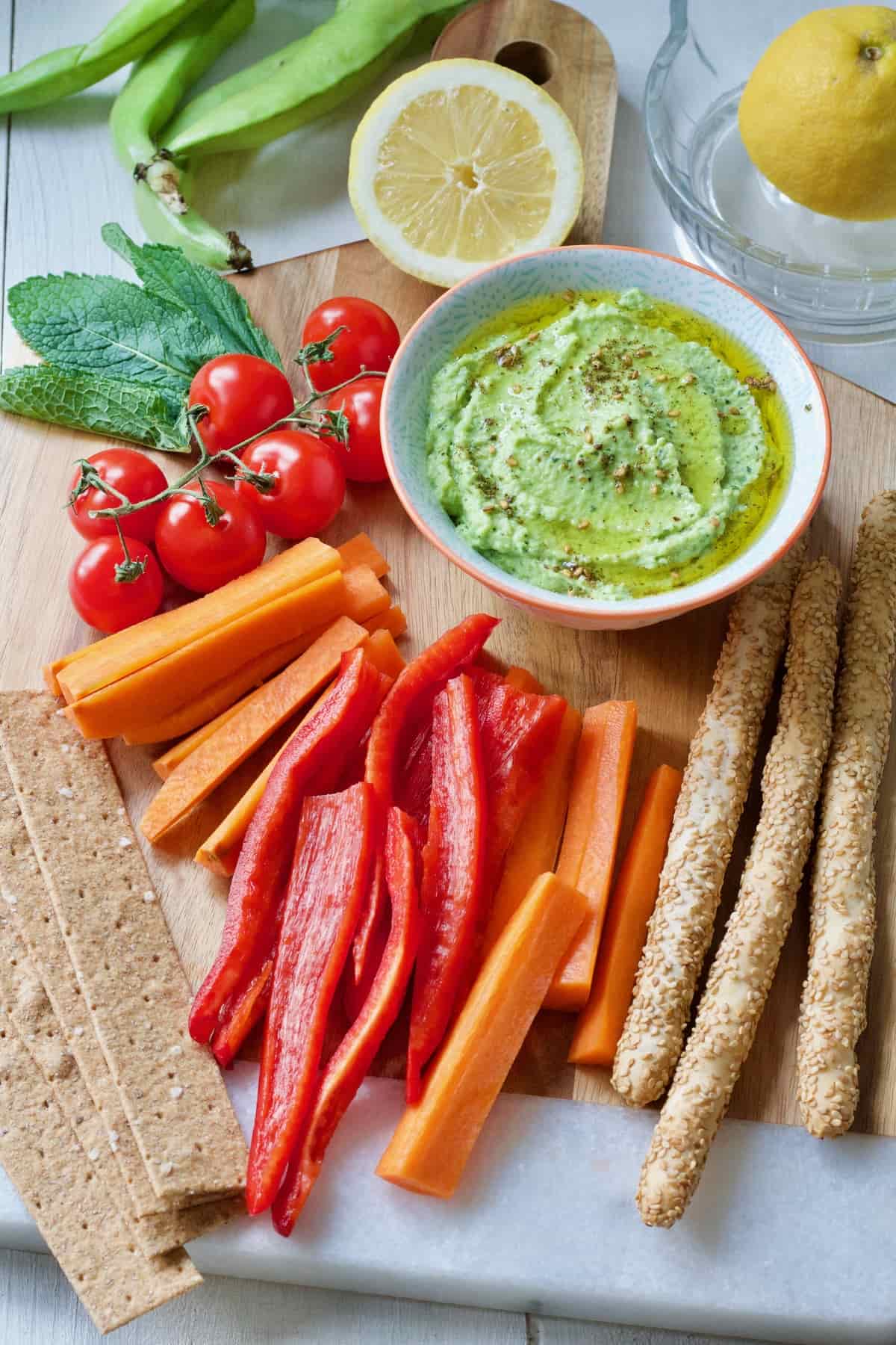 Crudites, crackers, tomatoes & green dip in a bowl.