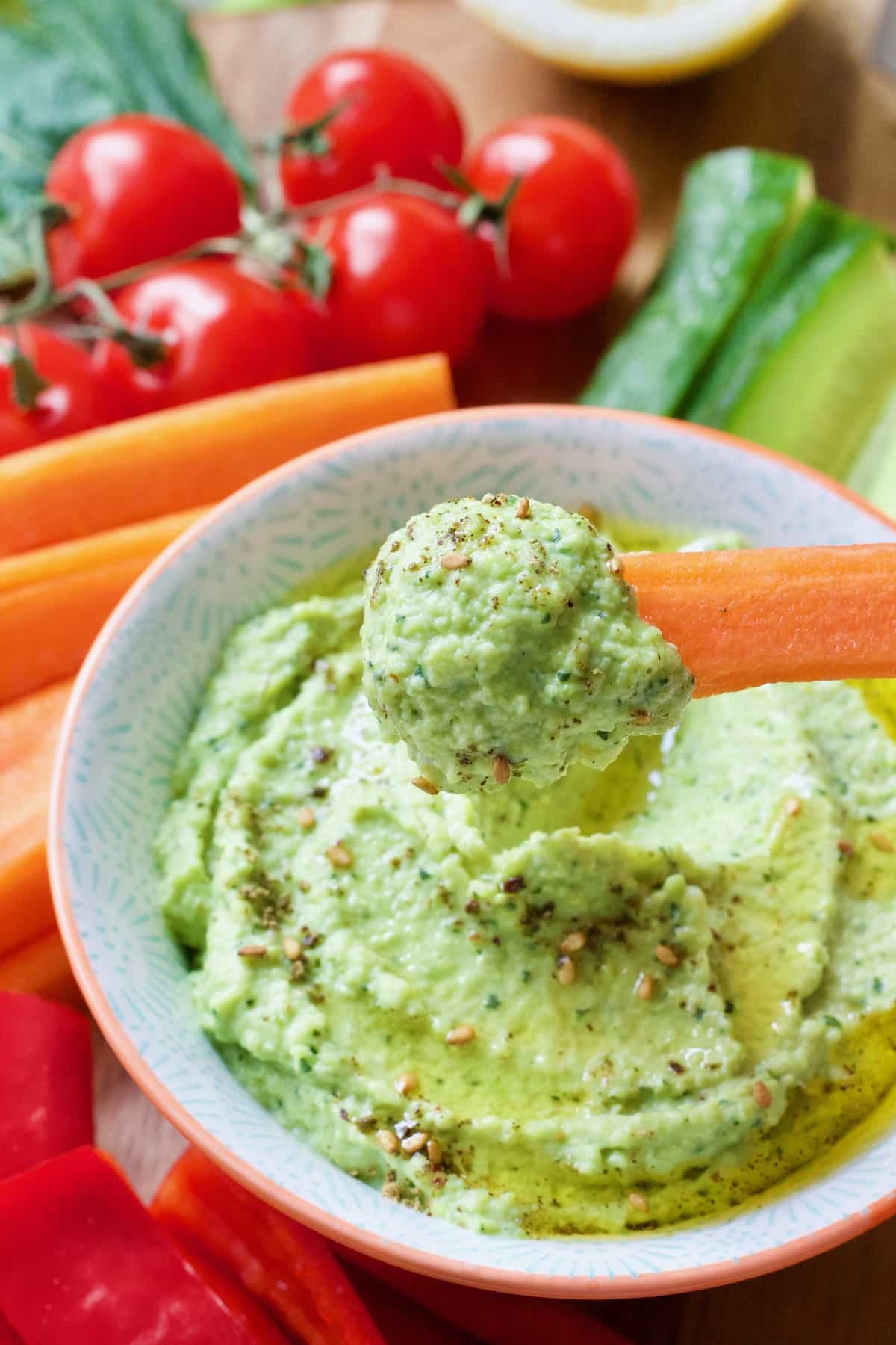 Broad bean dip on a carrot stick over a bowl.