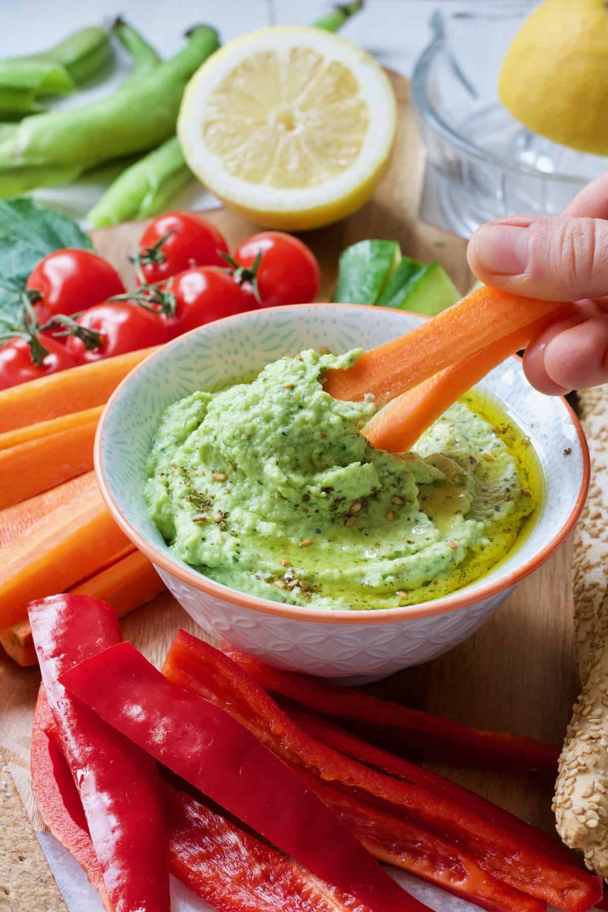 Two carrot sticks being dipped in a broad bean dip.