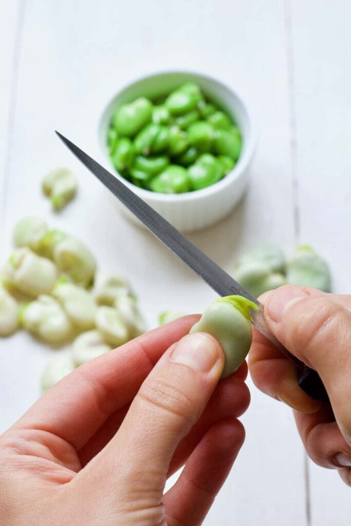 Knife about to cut the top of a broad bean.