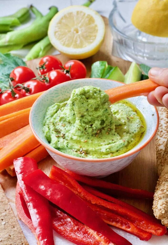 Carrot stick being dipped in broad bean dip.