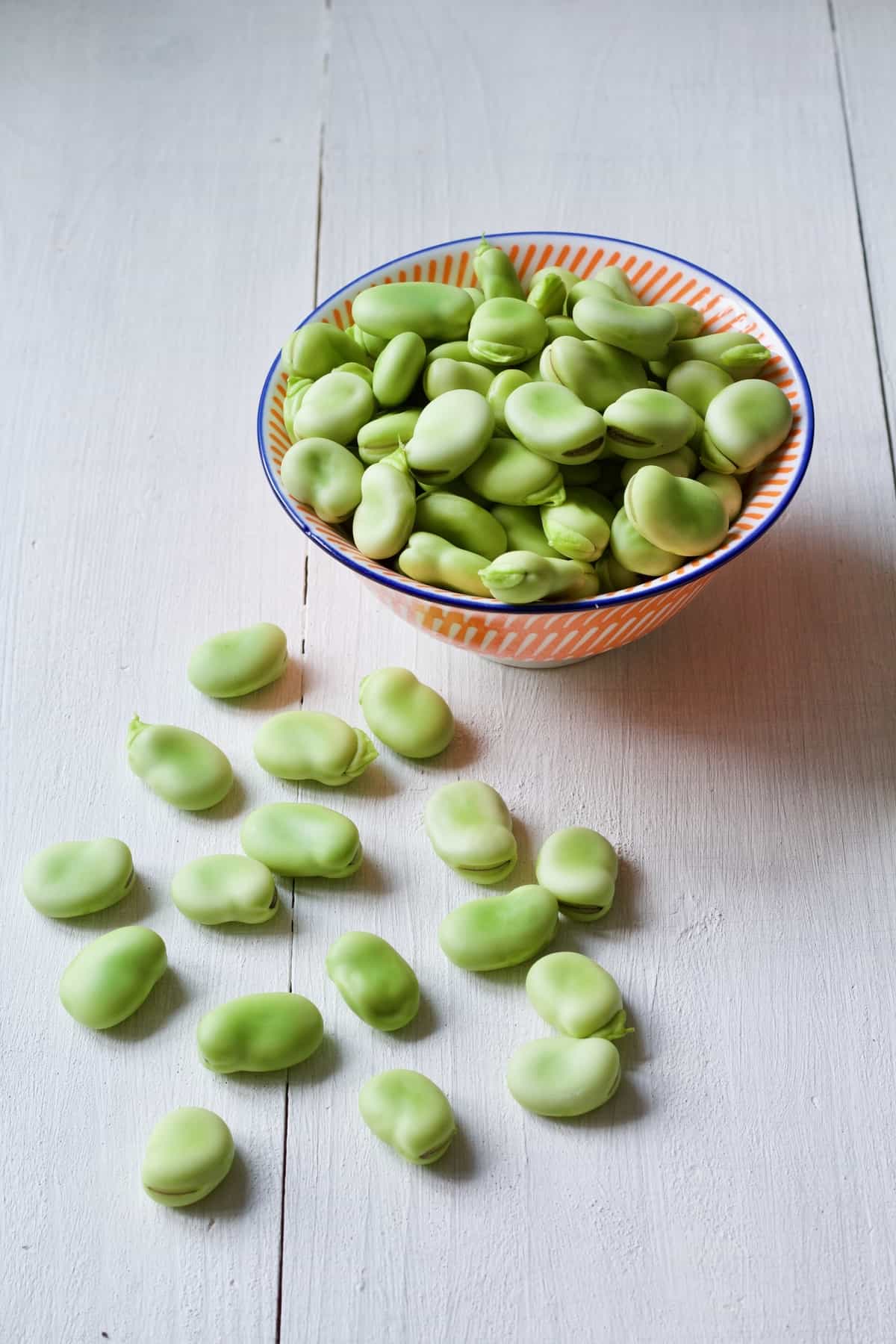 Skinned, raw broad beans in a bowl with some on a board.