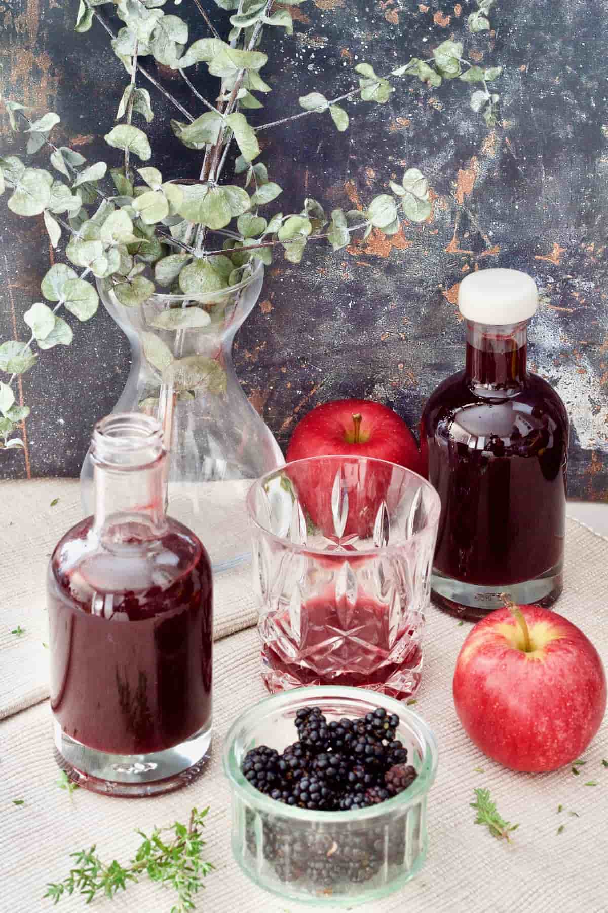 Bottles with vinegar, bowl with blackberries, tumbler and apples.