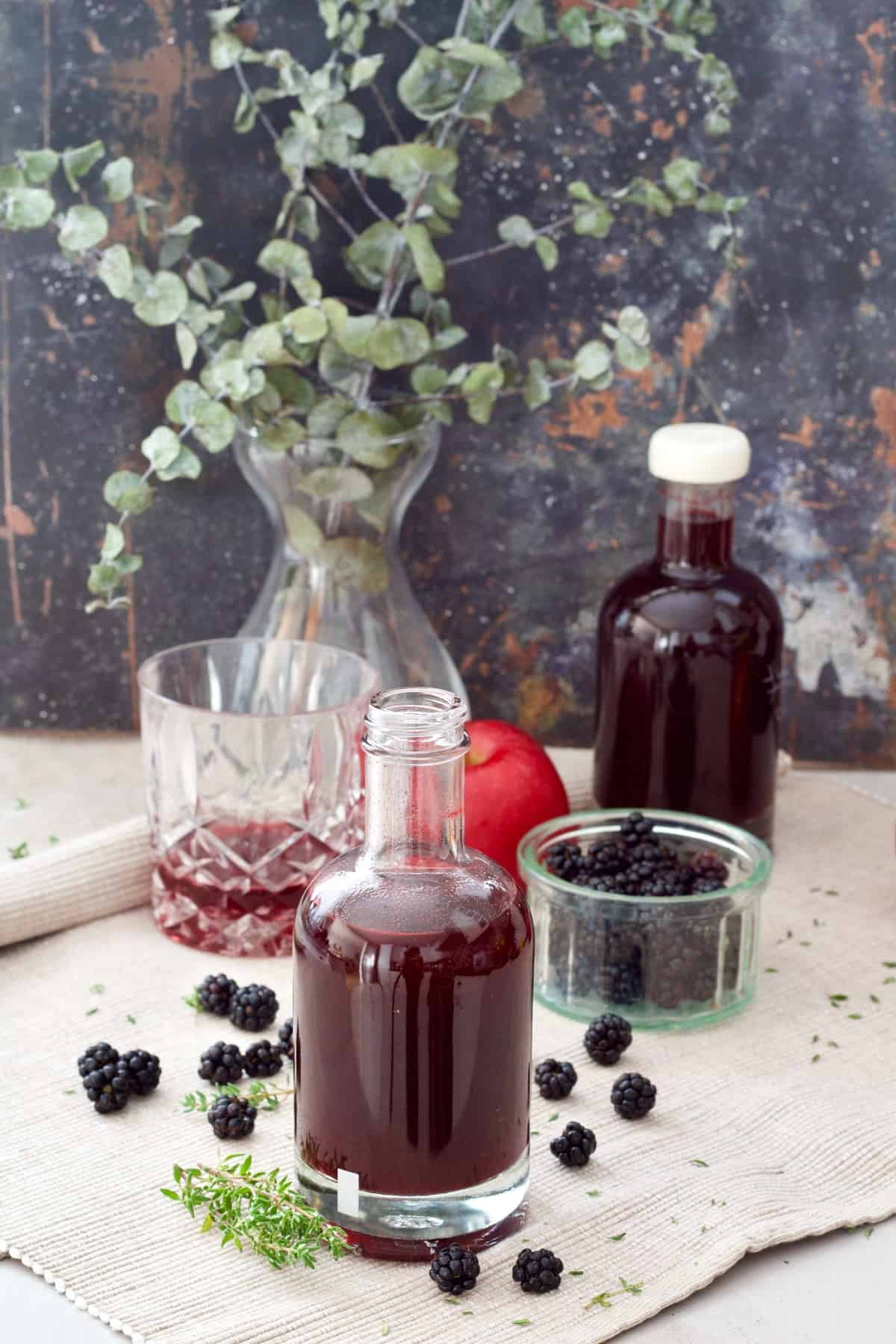 Open bottle of vinegar and scattered blackberries.