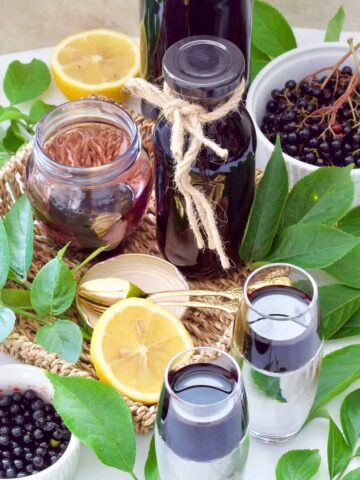 Fresh elderberries, green leaves & juice in bottles & glasses.