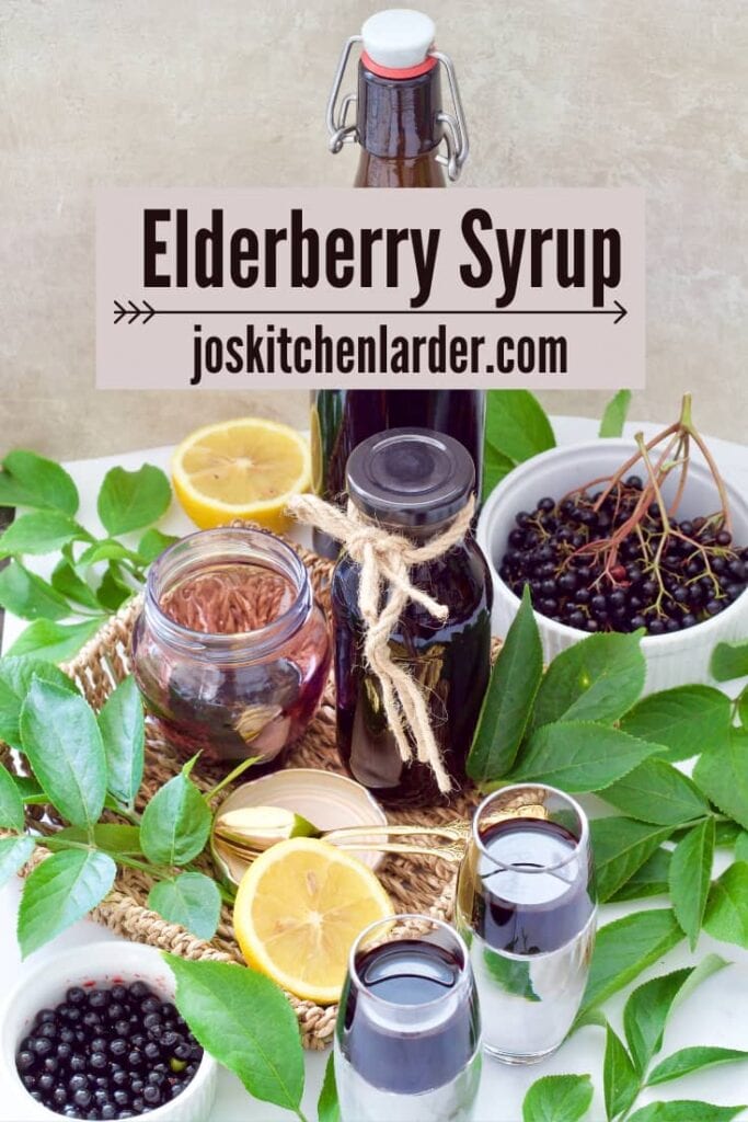 Elderberry syrup in bottles & shot glasses, fresh berries & leaves.