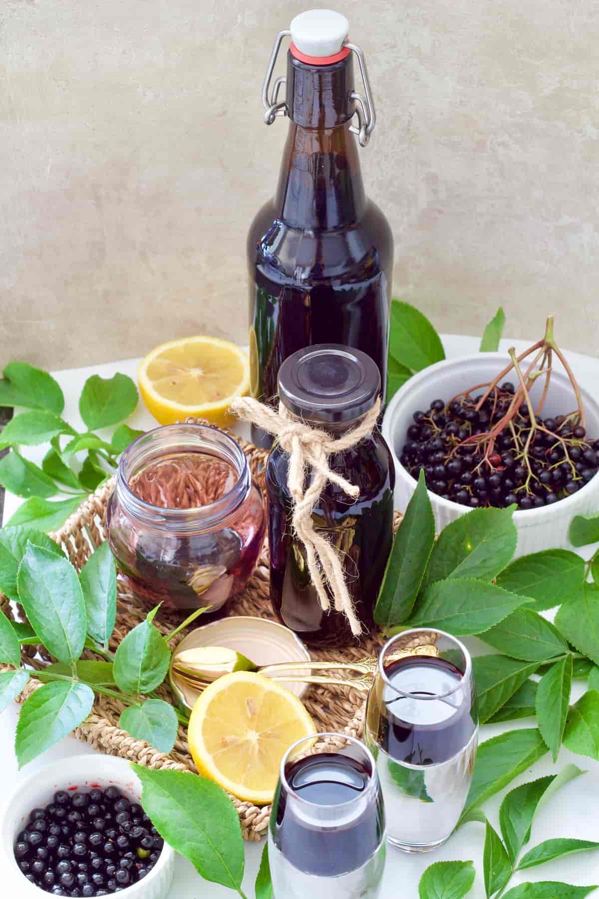 Fresh elderberries, leaves & syrup in bottles, jar & shot glasses.