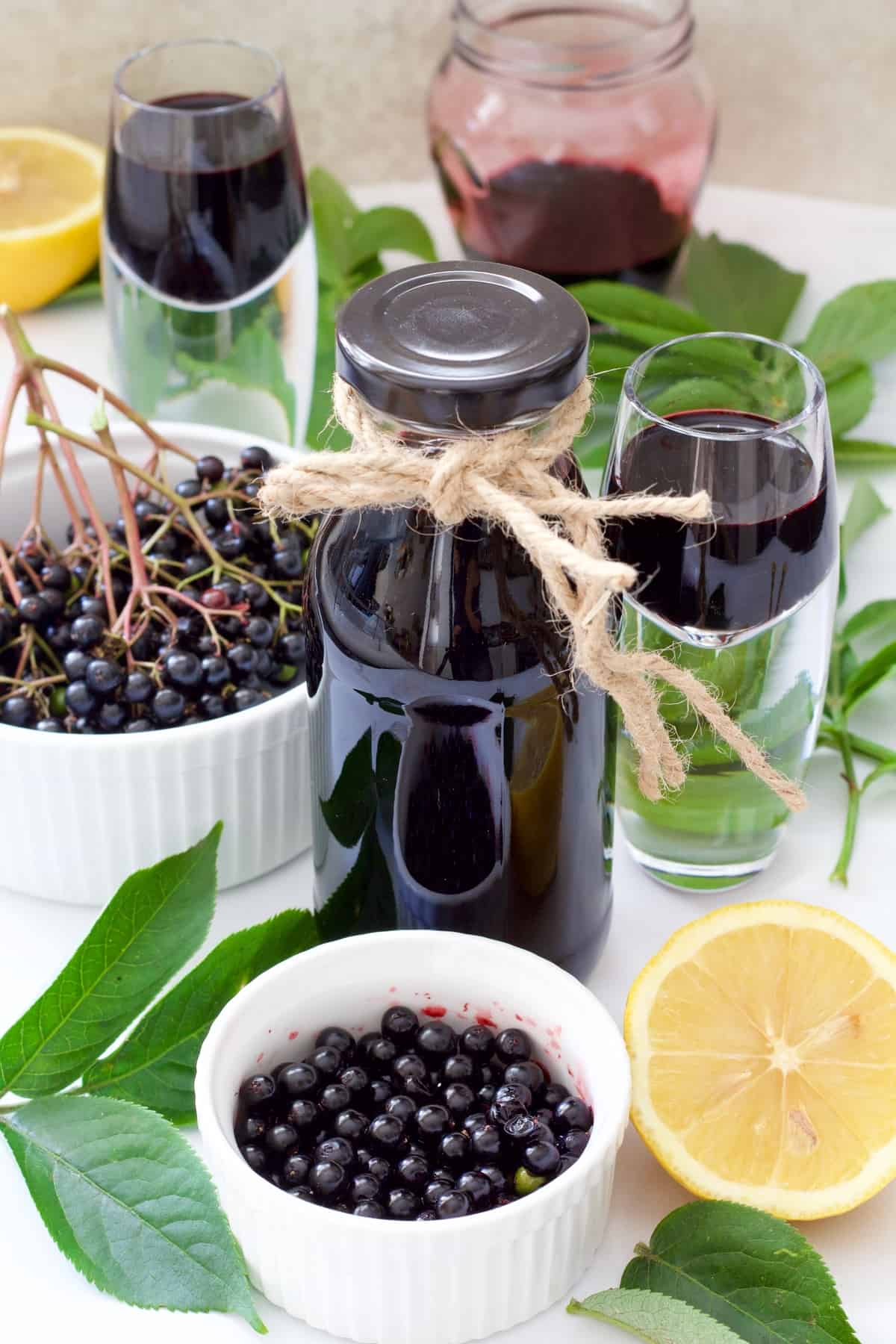 Fresh elderberries in bowls, syrup in bottle and shot glasses.