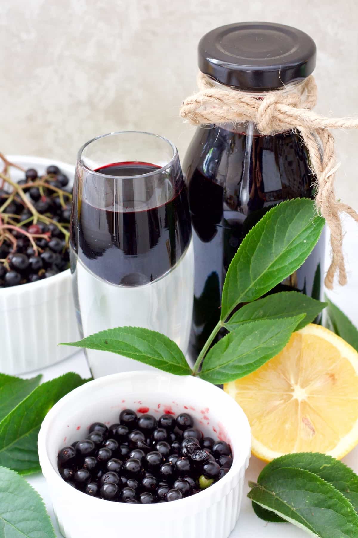 Small bottle & shot glass w with elderberry syrup, fresh elderberries.