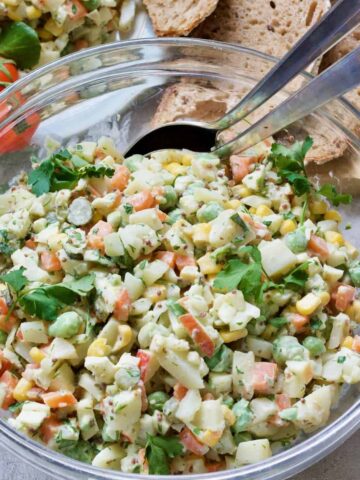 Russian salad in a bowl with serving spoons.