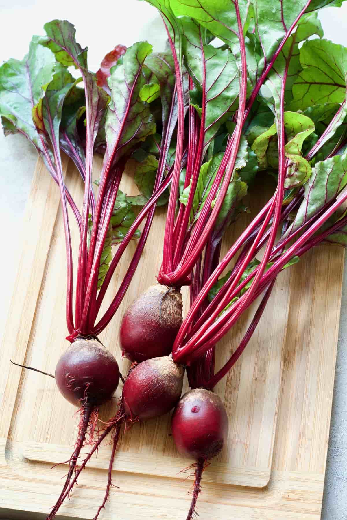 Bunch of young beets with greens on a board.