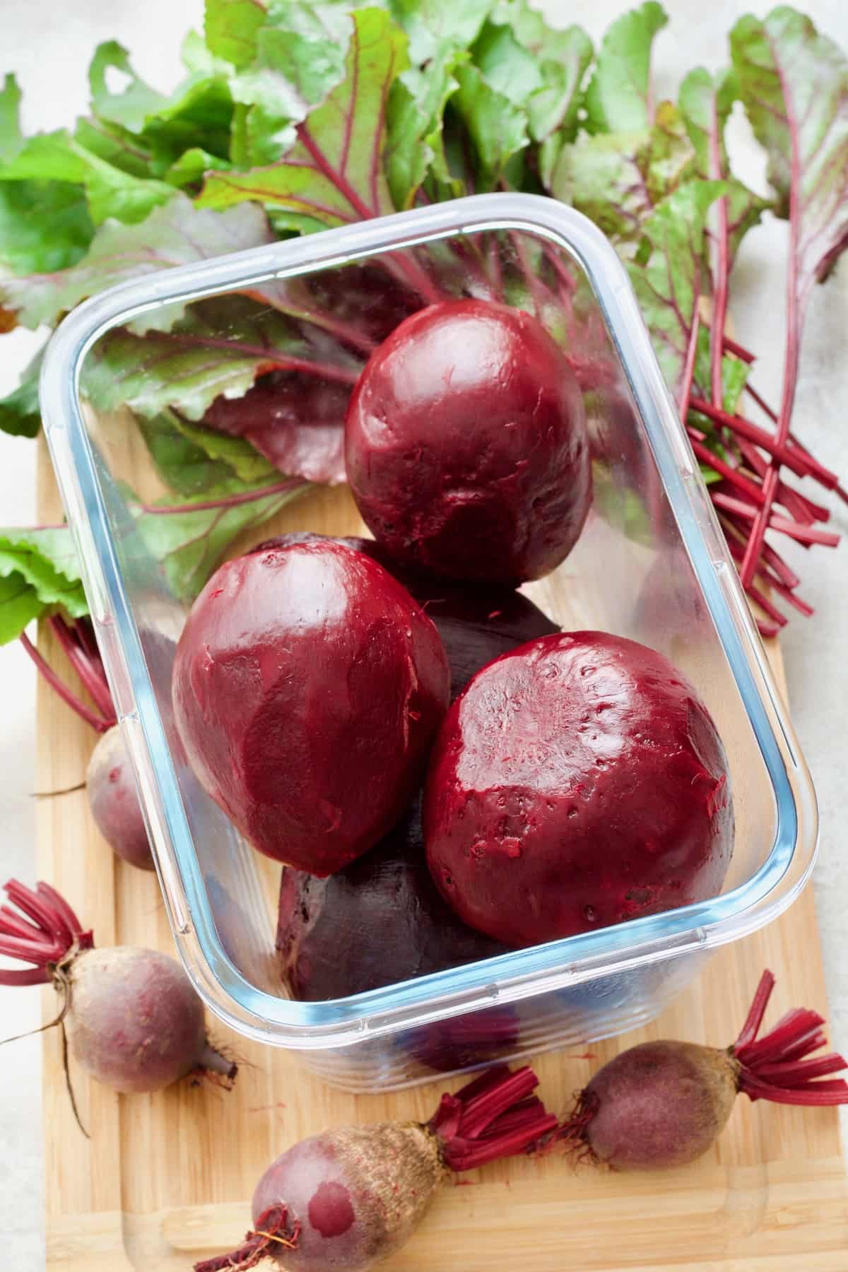 Cooked and peeled beets in a container, small raw beets around.