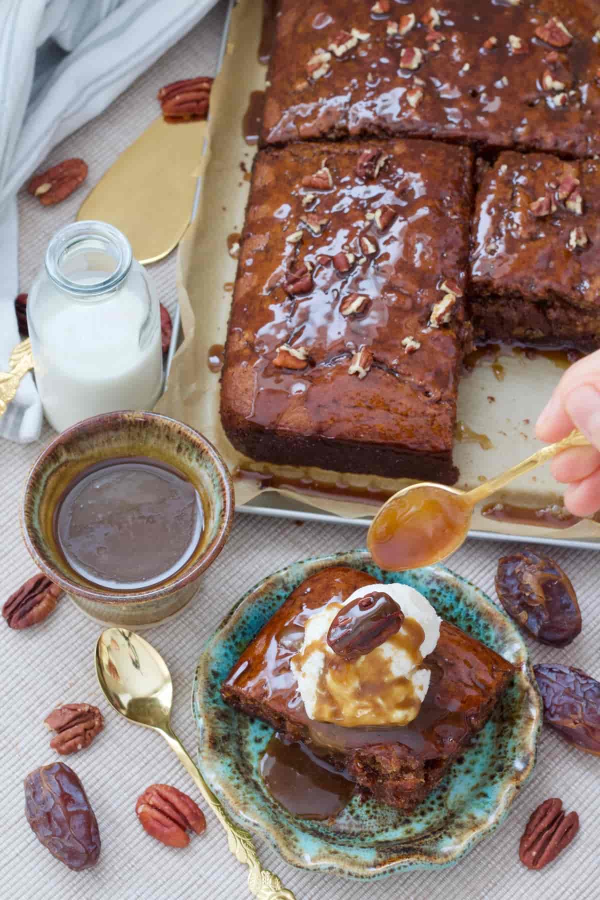 Hand holding spoon with toffee sauce over portion of pudding.