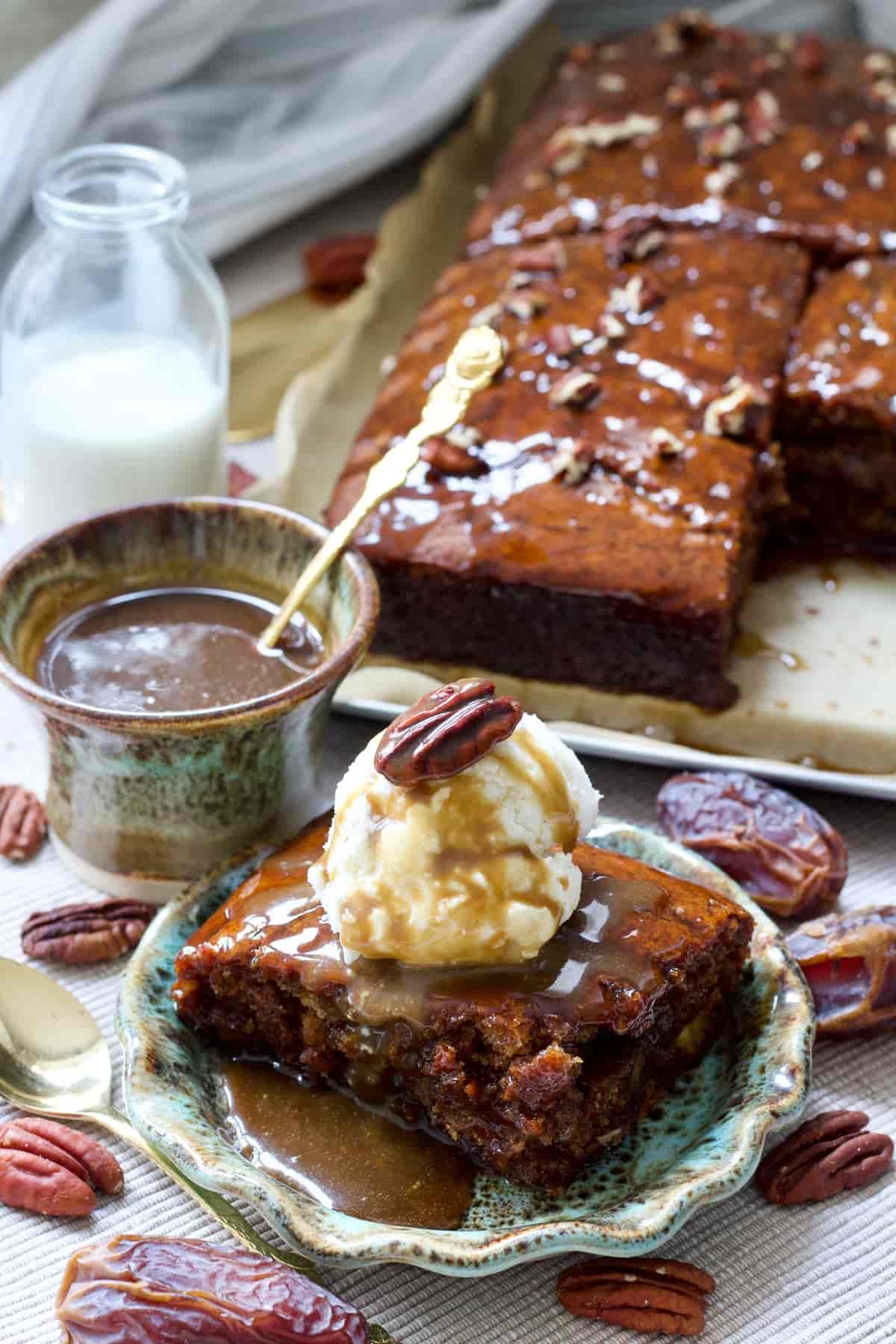 Portion of pudding with ice cream, toffee sauce in a bowl and more pudding behind.