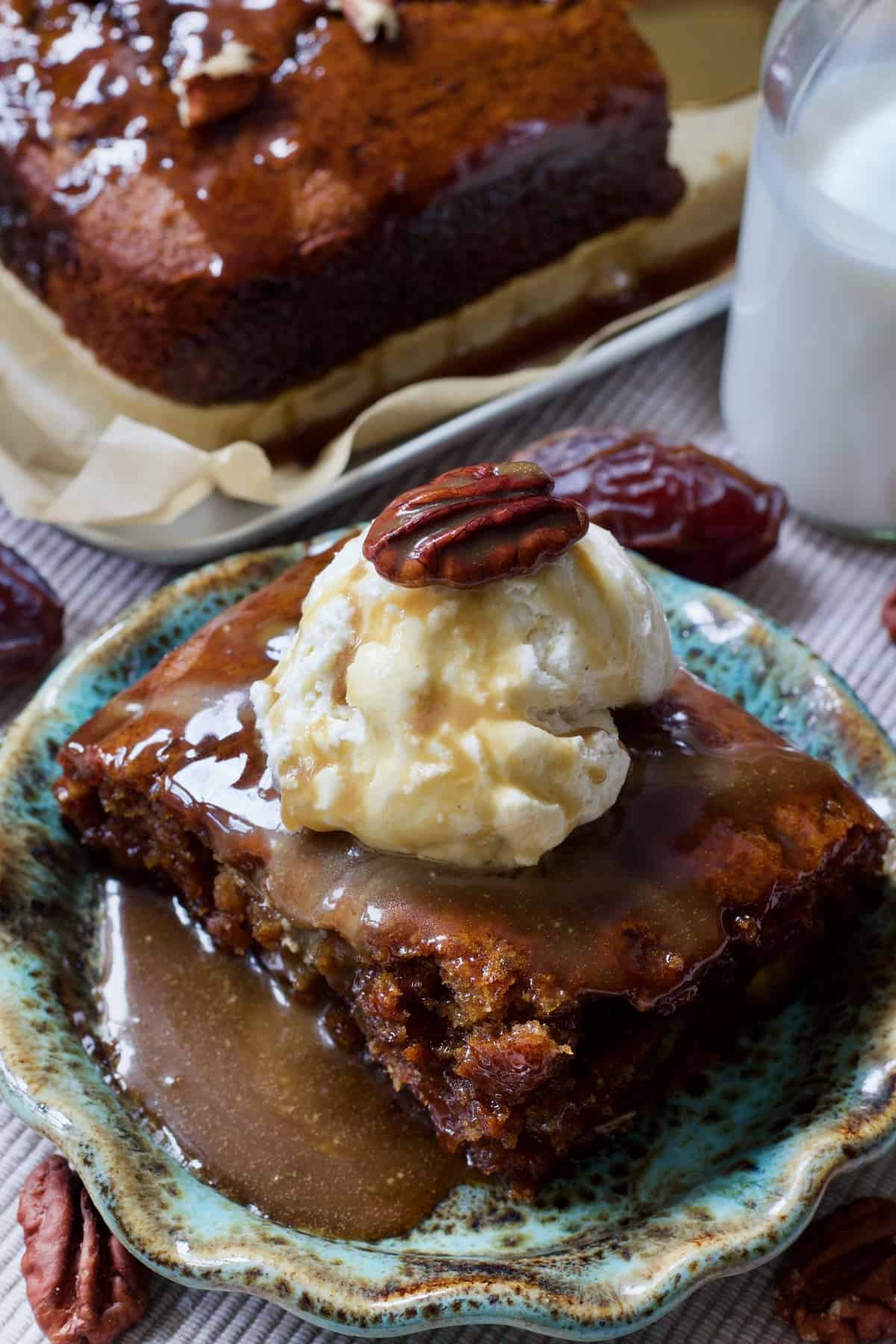 Vegan sticky toffee pudding on a plate with ice cream, toffee sauce and pecan nut.