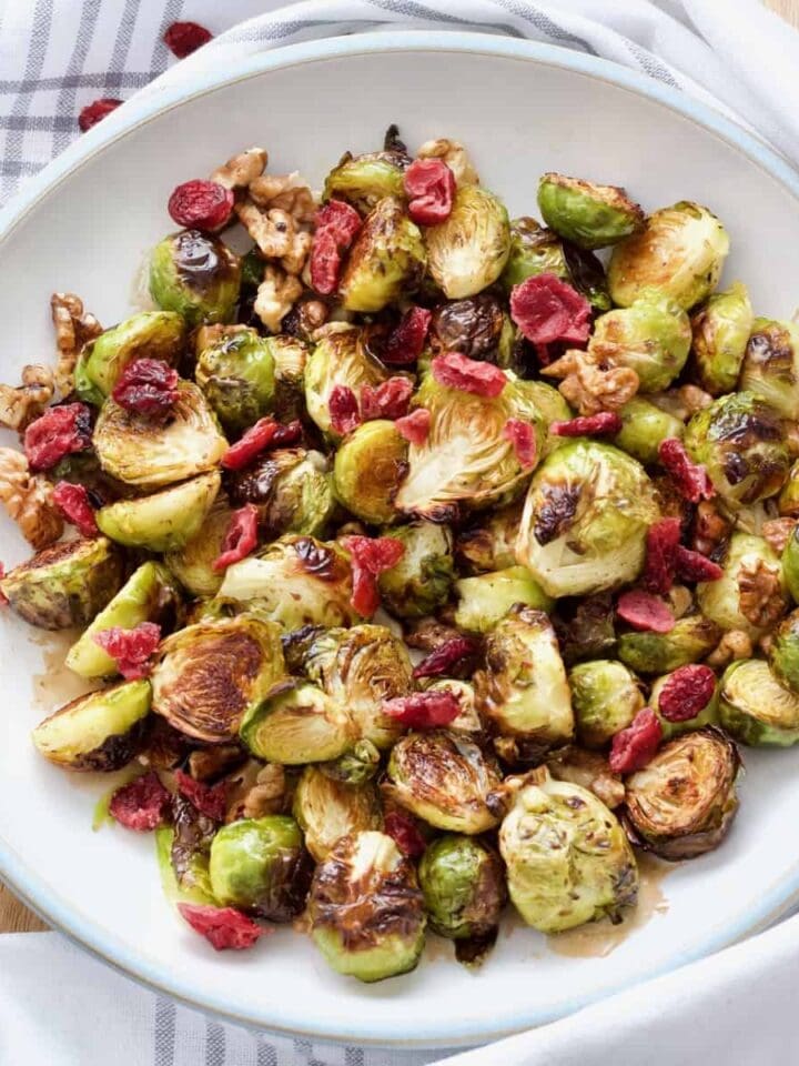 Bowl with roasted Brussels sprouts with balsamic vinegar and walnuts topped with cranberries.