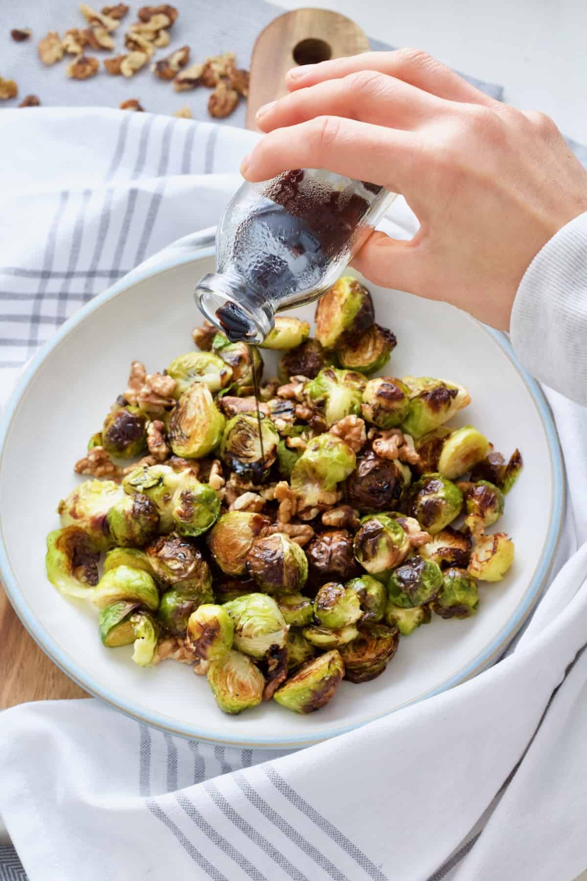 Hand pouring balsamic vinegar & maple reduction over roasted Brussels sprouts.